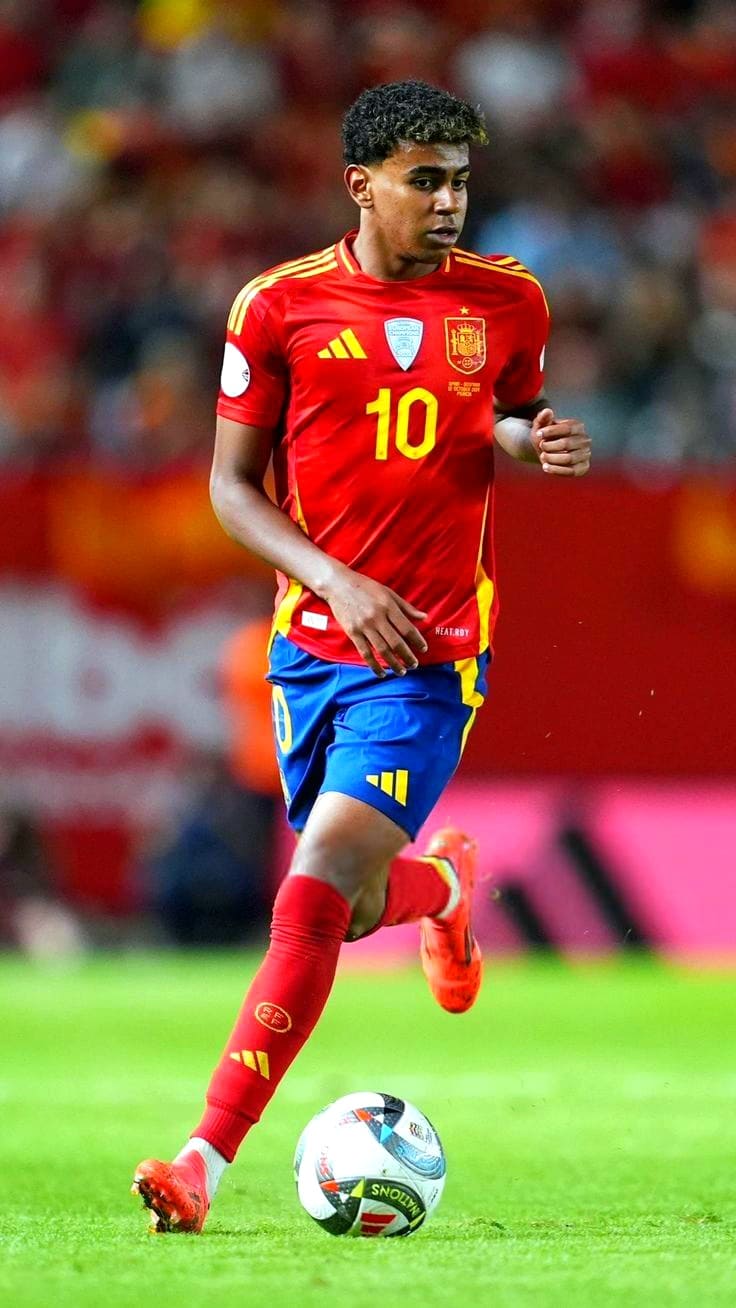 A male soccer player in a red and yellow Spain jersey with number 10 is running on the field, focusing on the ball at his feet. The background shows blurred fans in a stadium, capturing the excitement often streamed live through Brasil IPTV services.