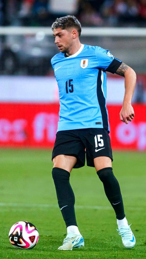 A soccer player in a light blue jersey with the number 15 controls a ball on the field during a match, as fans watch through Brasil IPTV for live coverage.