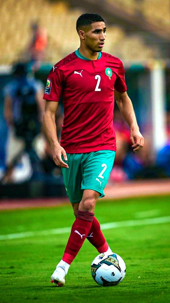 A soccer player in a red and green Morocco uniform with the number 2 on his shirt controls a ball on a field during a match, captured live through IPTV BrasiL coverage.