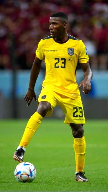 A soccer player in a yellow uniform with number 23, standing on grass and controlling a ball during a match. The background shows a stadium with blurred spectators, capturing the energy and excitement often streamed live on Brasil IPTV.